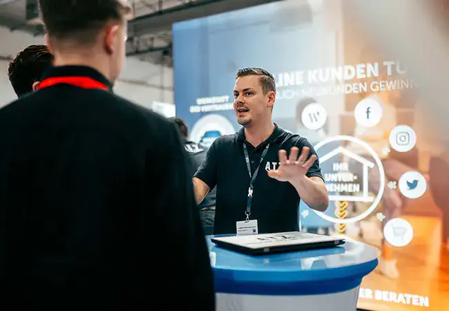 ATZ Group sales employee talking to visitors at a trade fair stand